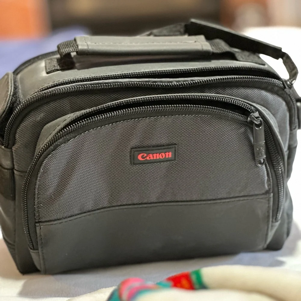 Canon black camera bag with zipper packets, and a handle at the top.
